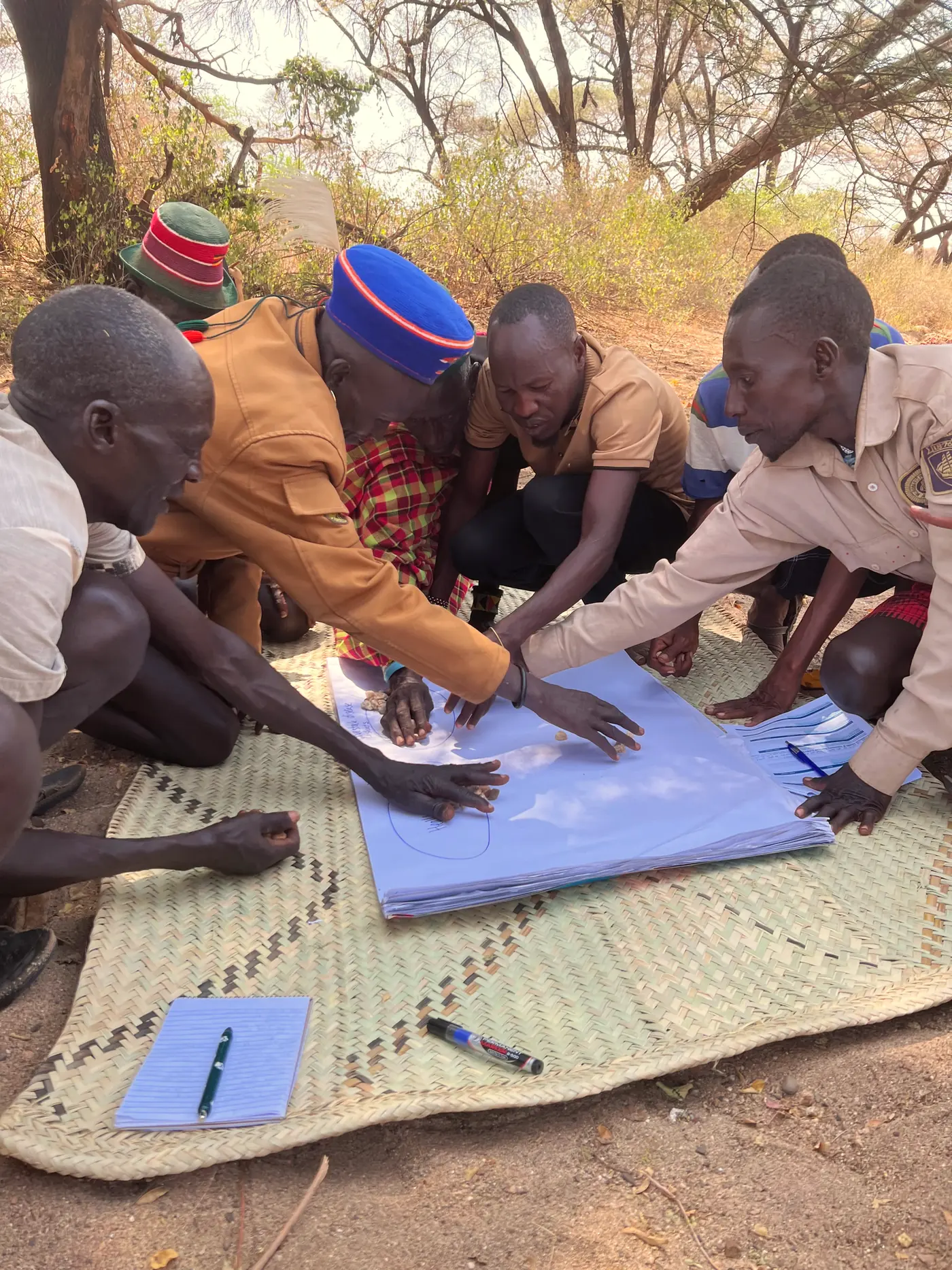 Men lean over a paper chart placing stones during a COHI focus group.