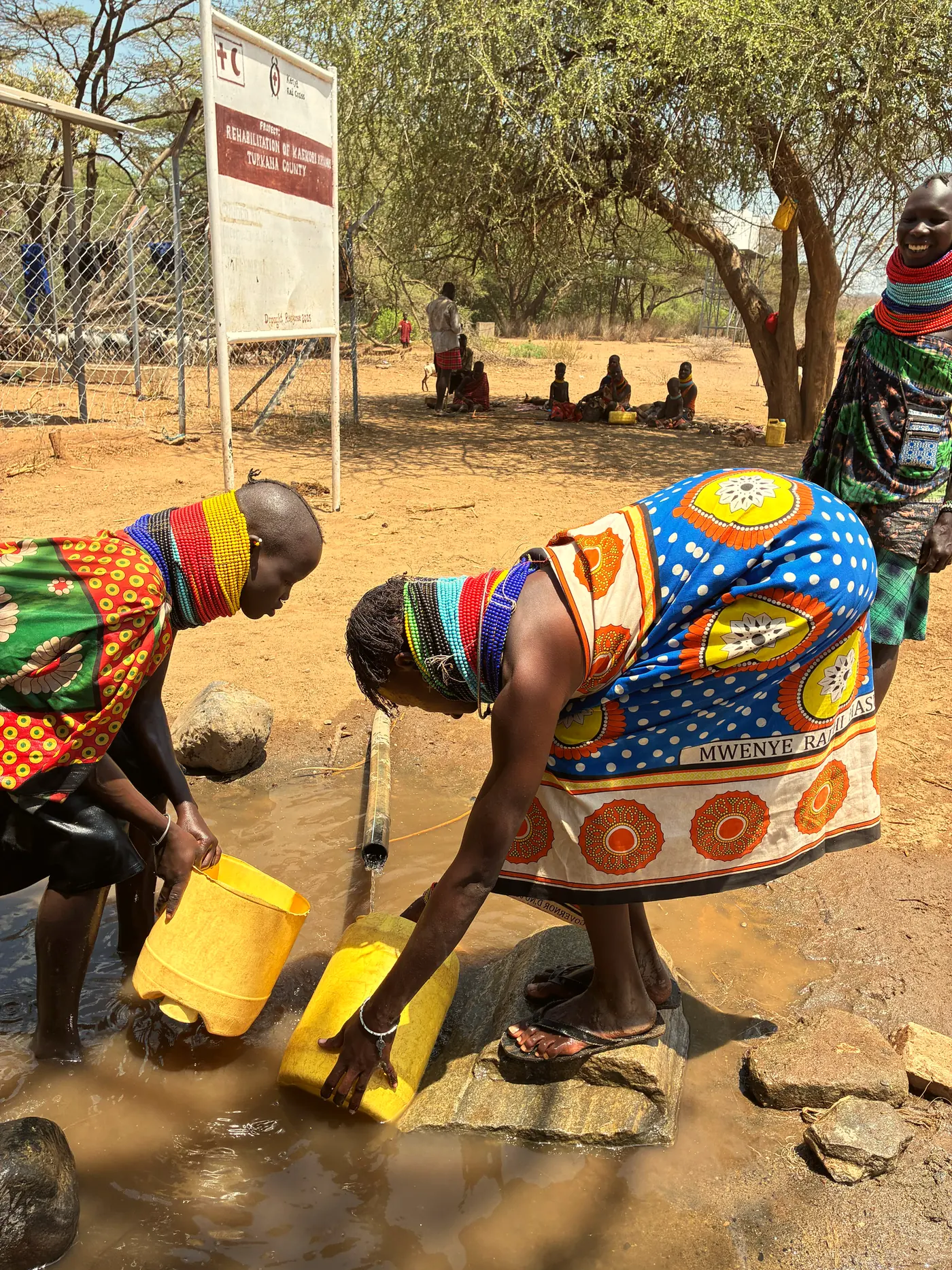 Women collect water from a pipe into yellow jerrycans.